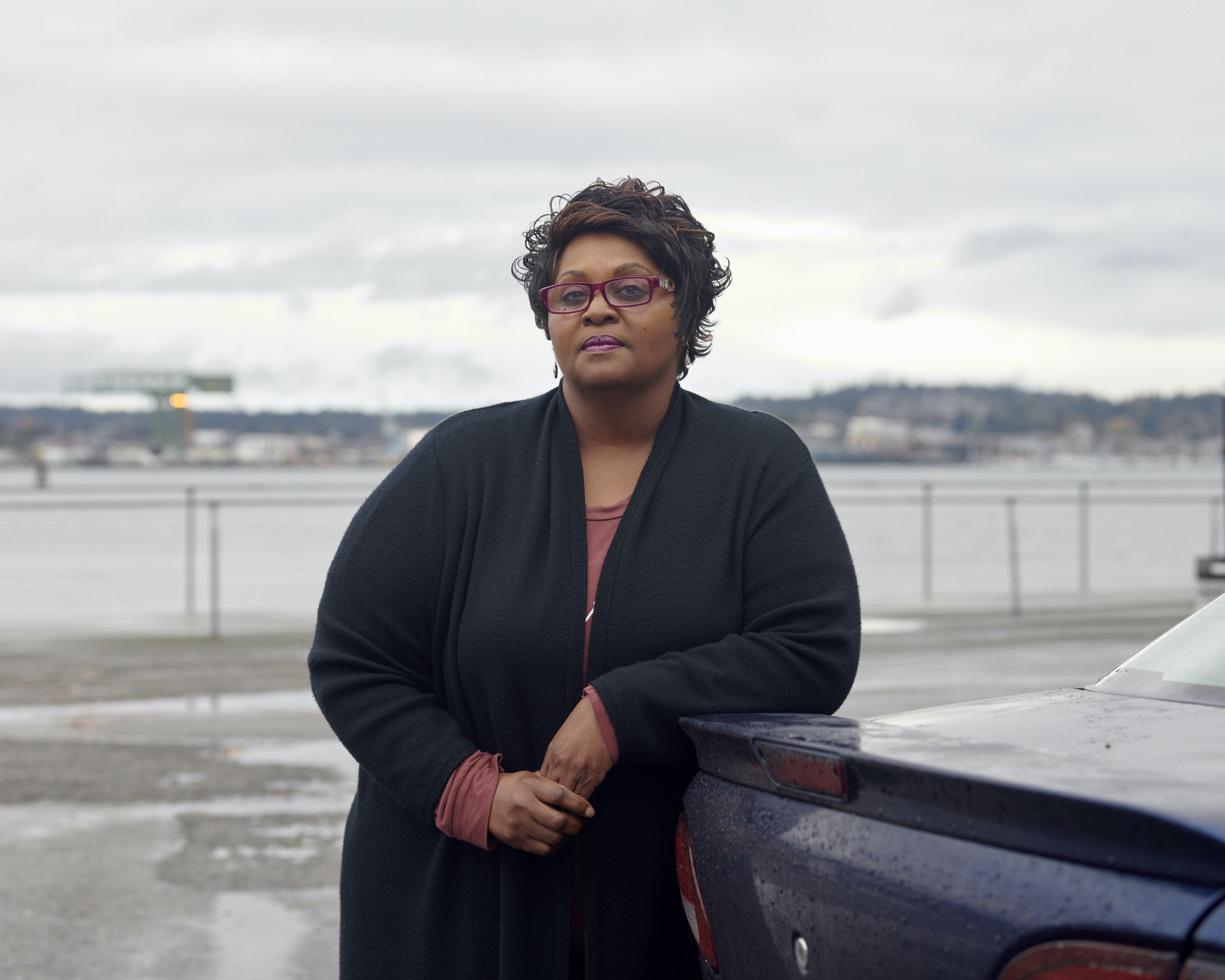 Portrait of a woman standing near a waterfront, looking directly into the camera.